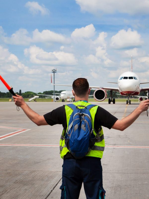 The traffic controller at the airport shows the semaphore with sticks to the pilot of the plane where to park. Arrival of the plane on the runway. Handling service
